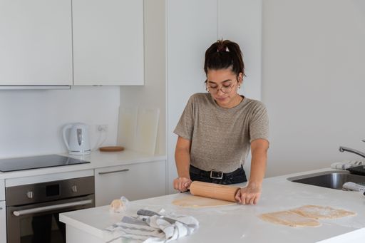 a young black haired woman cooking happy homemade pasta by hand with rolling pin