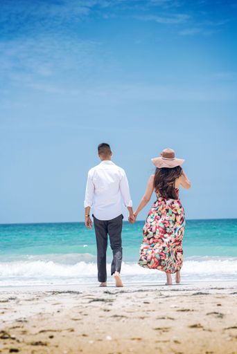 A vertical of a couple walking on the beach, holding hands on a sunny day