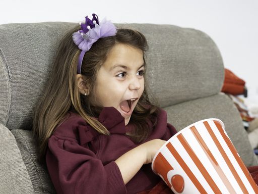 A Latina girl screaming while watching a movie in her living room with a popcorn pot