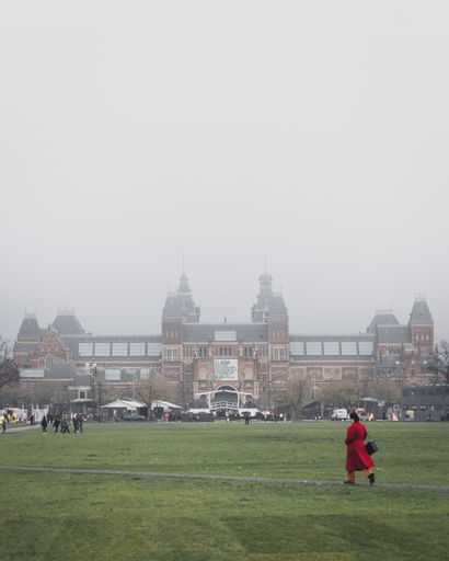 A lady in a red coat crossing parkland in front of the Rijksmuseum on a misty autumn morning in Amsterdam, Netherlands