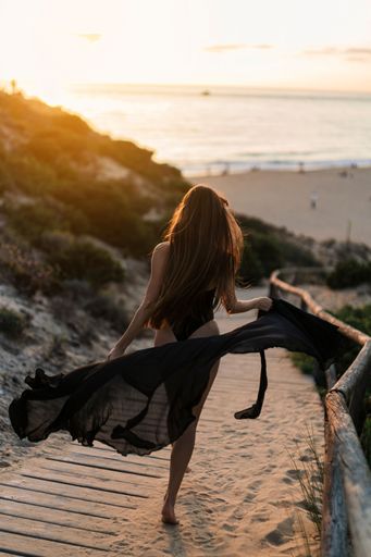 A woman walking along a beach path illuminated by the orange and pink hues of a picturesque sunset.
