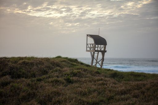A lifeguard tower in a field surrounded by the sea under a cloudy sky in the evening