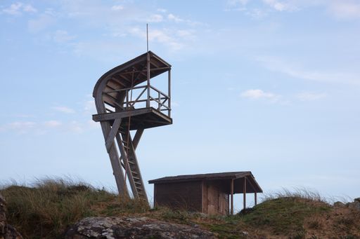 A lifeguard tower in a field surrounded by the sea under a cloudy sky in the evening