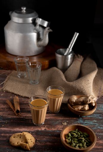 A wooden table with an antique kettle, ceramic bowls and mugs on it, against a black background