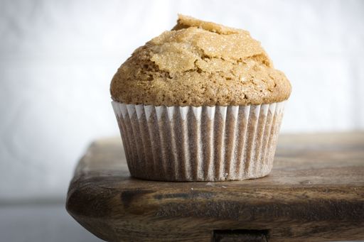 A delicious and freshly-baked muffin placed on a rustic wooden countertop, with a side view of the top of the muffin in full focus