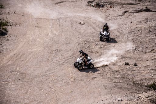 The two people  wearing helmets and drifting on the sandy field with quad bike