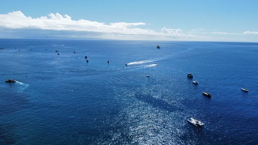 An aerial view of boats sailing in the sea near the shore on a sunny day