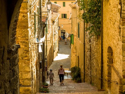 Two people are walking down a cobblestone street in the Italian town of Suvereto, Tuscany
