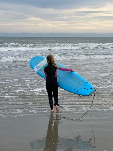 A female surfer stands on the beach, her blue surfboard at her side