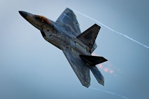A modern military jet fighter aircraft gliding through an azure sky, producing a white trail of smoke from its engines