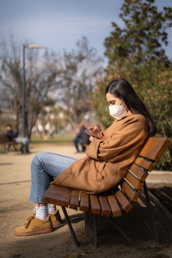 A young woman with a disability sitting on a park bench using a digital tablet for work