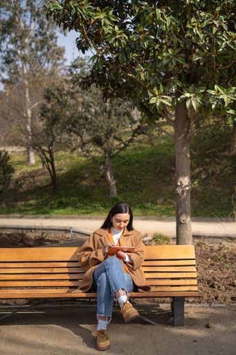 A young woman with a disability sitting on a park bench using a digital tablet for work