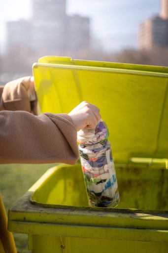 A woman with disability in hand throwing a plastic bottle into green trash bin