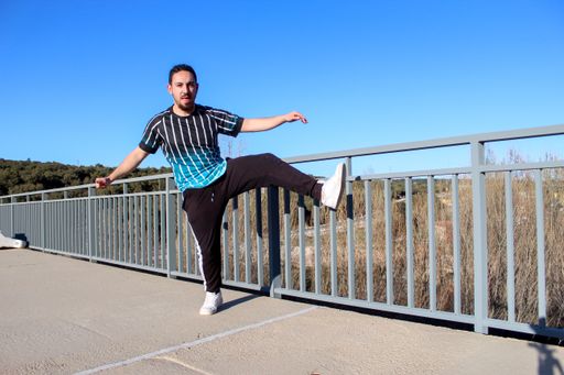 A young and positive male with braids in his hair dancing an urban dance on the bridge