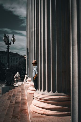 A vertical shot of a man in hat standing between columns of an old high building
