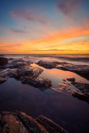 A spectacular sunrise over a serene ocean landscape, with a beach and rolling waves visible at low tide