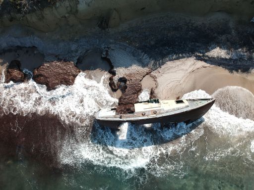 An aerial view of an old boat on the shore surrounded by picturesque rocky outcroppings