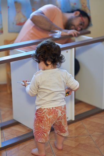 A Hispanic son plays while his father assembles wooden furniture at home