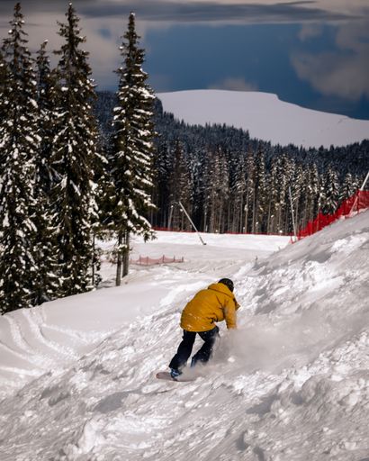 A vertical shot of an adult person with a helmet snowboarding on the hills in a resort area
