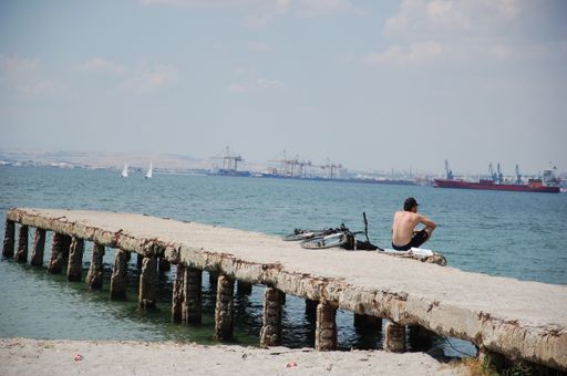 A young man sitting on the pier with his bicycle laid on a concrete surface