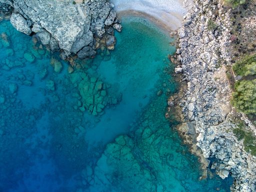An aerial view of a coastal featuring a rocky shoreline and beautiful blue waters