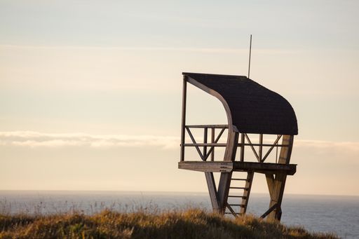 A lifeguard tower in a field surrounded by the sea under a cloudy sky in the evening
