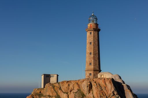 The Lighthouse of Cabo Vilan on rocks under the sunlight and a blue sky in Spain