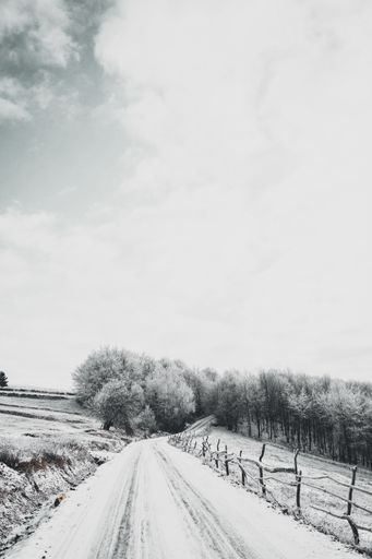 A vertical high angle shot of a snowy road leading to the forest