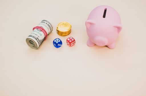 A piggy bank with dice, gold coins, and rolled up dollars next to it