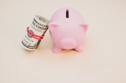 A piggy bank with rolled dollars leaning on it on a smooth table