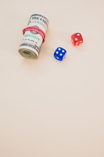 A vertical shot of red and blue dice next to rolled dollars on a smooth table