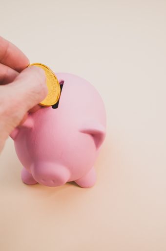 A vertical shot of a hand inserting a gold coin into a piggy bank