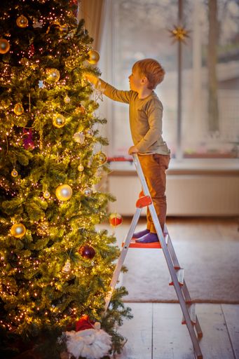 A vertical shot of a small boy hanging ornaments on the Christmas tree
