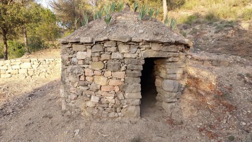 A traditional stone house situated near a mountainous landscape, featuring an open doorway for passers-by