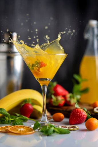 A vertical shot of a cocktail glass with fruit drink orange strawberries bananas and kumquats