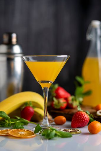 A vertical shot of a cocktail glass with fruit drink orange strawberries bananas and kumquats