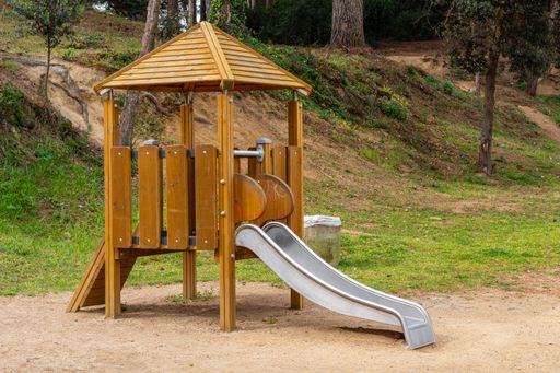 A wooden playground on the sand in the park at the foot of a hill on a sunny day