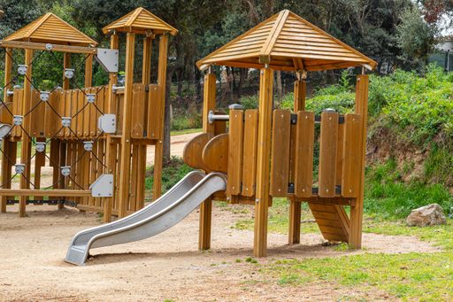 A wooden playground on the sand in the park at the foot of a hill on a sunny day