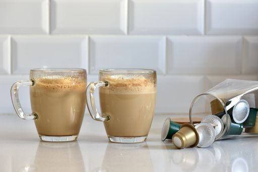 A closeup of two glasses of homemade cappuccinos with the capsules, on the white counter