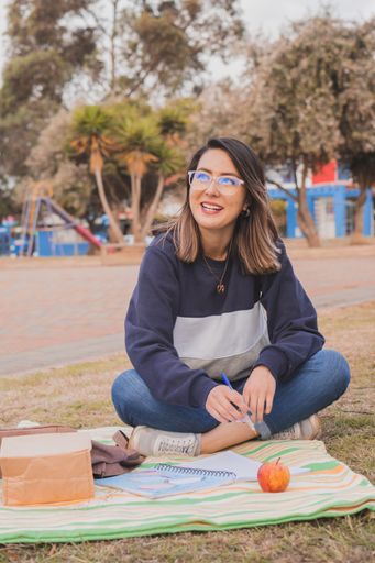 A female Hispanic college student sitting on the grass and studying in the park