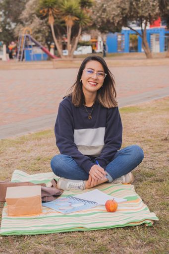 A female Hispanic college student sitting on the grass and studying in the park