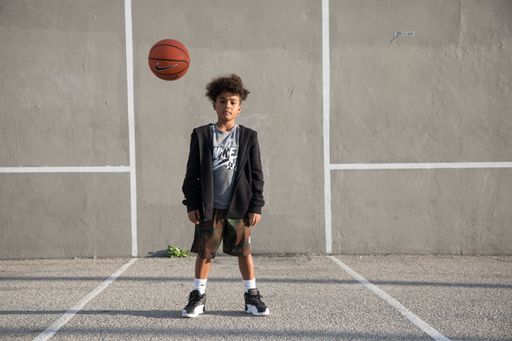 A cheerful young male stands outdoors, throwing a basketball up into the air