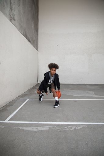 A cheerful young male stands outdoors, throwing a basketball up into the air