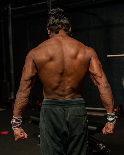 A shallow focus of an adult bodybuilder man with long hair showing his back muscles in a gym