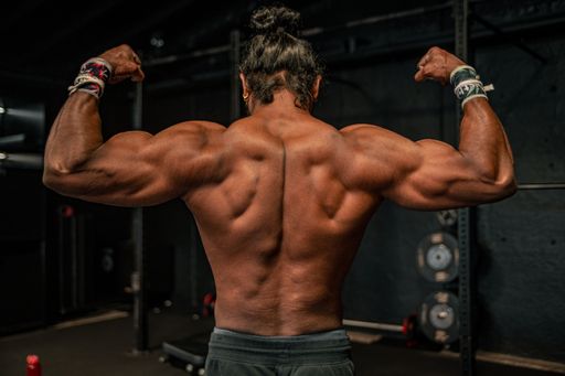 A shallow focus of an adult bodybuilder man with long hair showing his back muscles and biceps in a gym