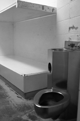 A vertical shot of a stainless steel toilet bowl and sink inside a prison cell