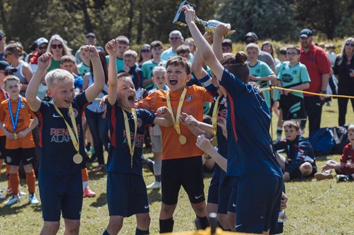 A group of children standing in celebration holding a medals above their heads in triumph