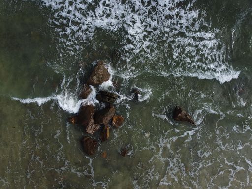 Aerial shot of waves crashing into rocks near the shore at close to high tide.