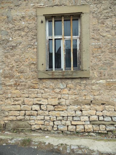 A white metal rusty lattice on the window of the old stone building