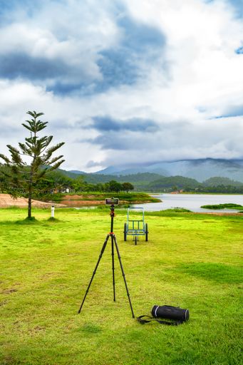 A professional photographer has set up their camera and tripod in a grassy outdoor field, with a tranquil body of water in the background